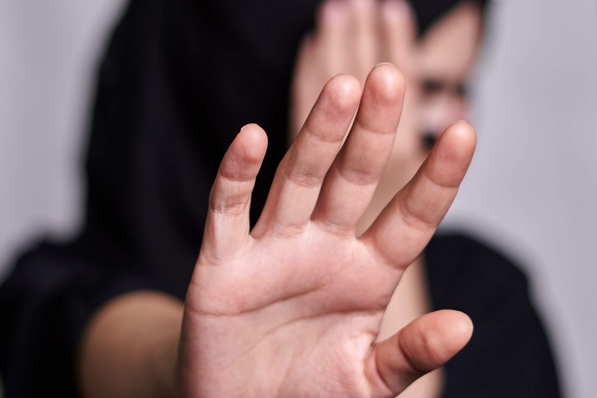 Person holds hand up, palm facing forward, covering face, blurred background. Person holds hand up, palm facing forward, covering face, blurred background.