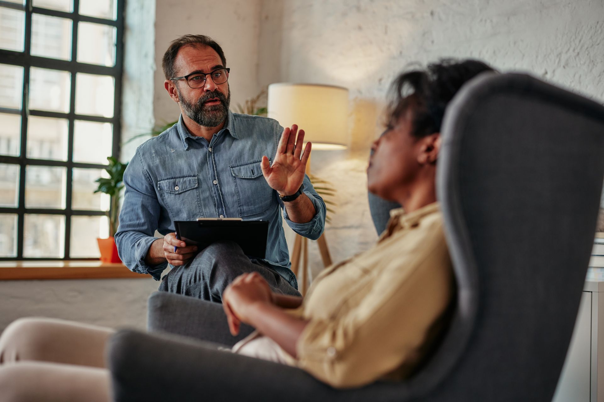 Therapist gesturing while talking to a client in an armchair in a sunlit room. Therapist gesturing while talking to a client in an armchair in a sunlit room.