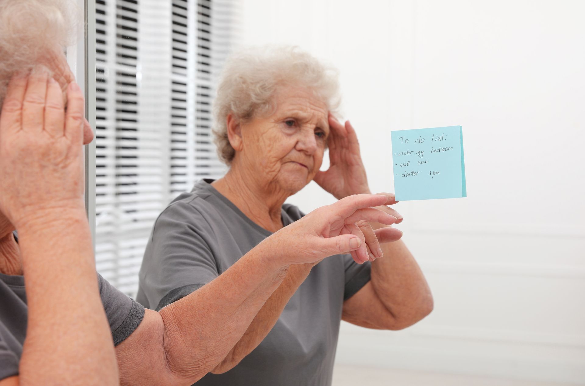 Woman looking in mirror with a post-it note, appearing confused. Woman looking in mirror with a post-it note, appearing confused.
