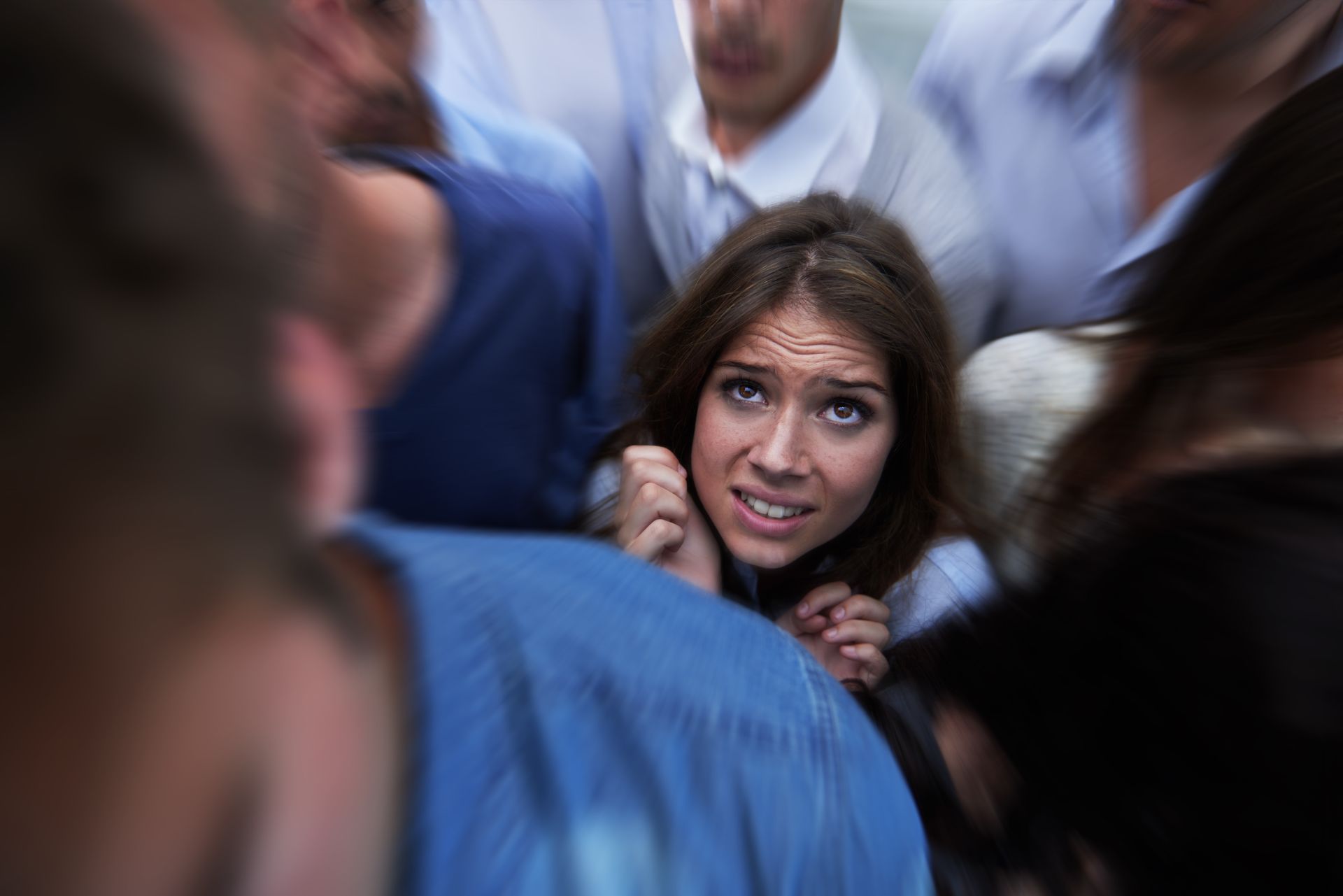 Woman with a panicked expression in a crowd of people, hands clenched.