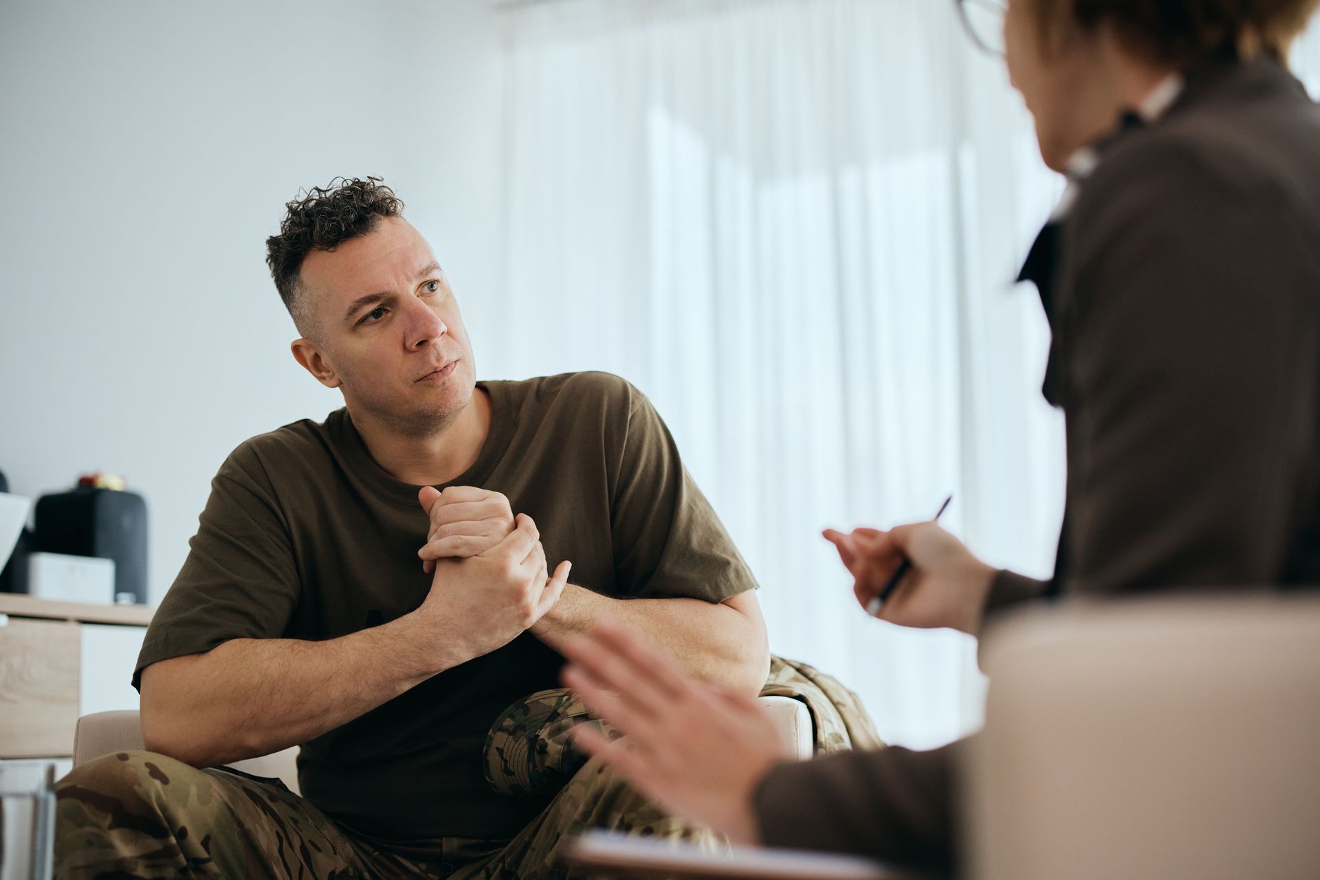 Man in military fatigues talking to a therapist in a brightly lit room. Man in military fatigues talking to a therapist in a brightly lit room.