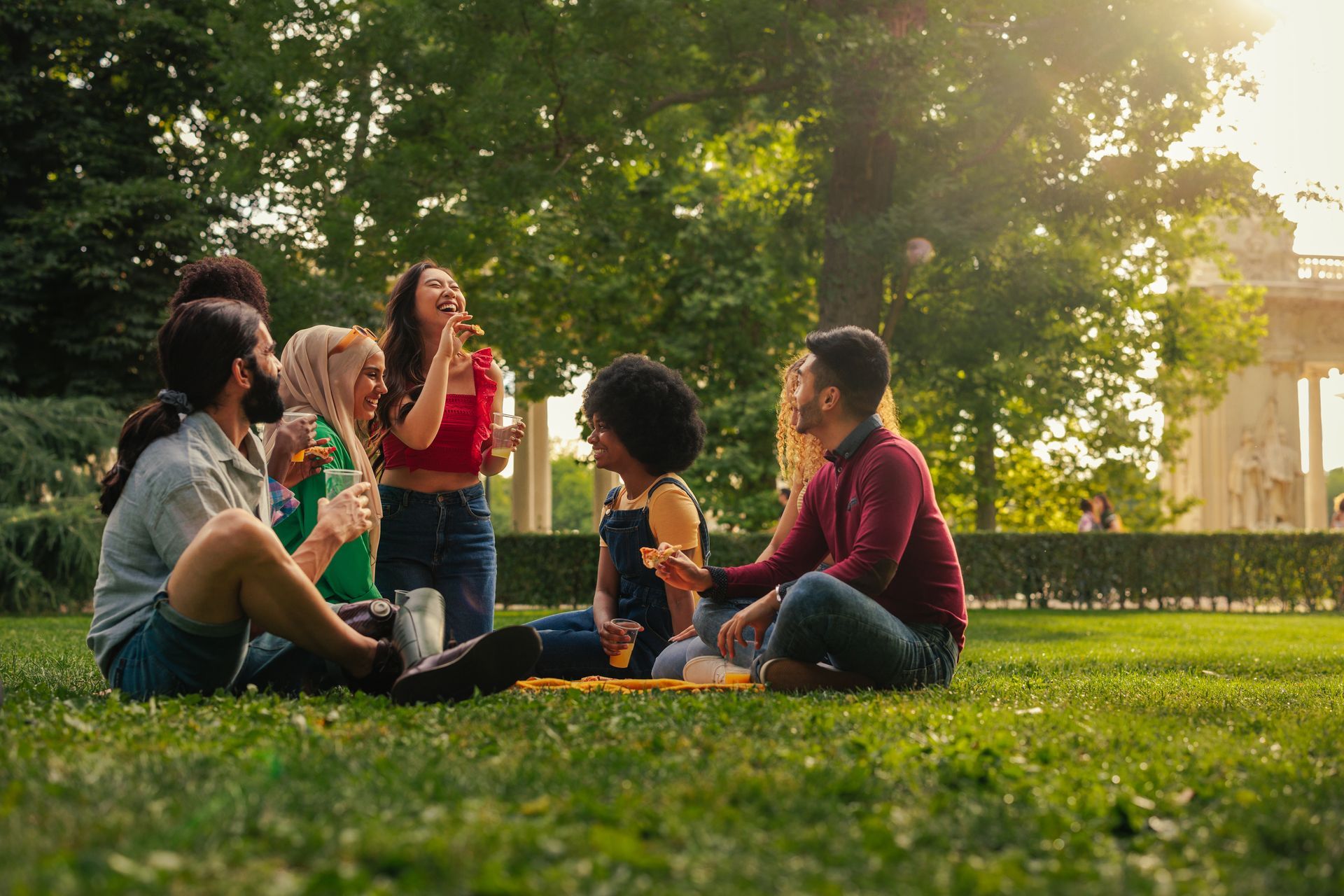 Group of people in a sunny park, seated on the grass, eating and smiling. Group of people in a sunny park, seated on the grass, eating and smiling.