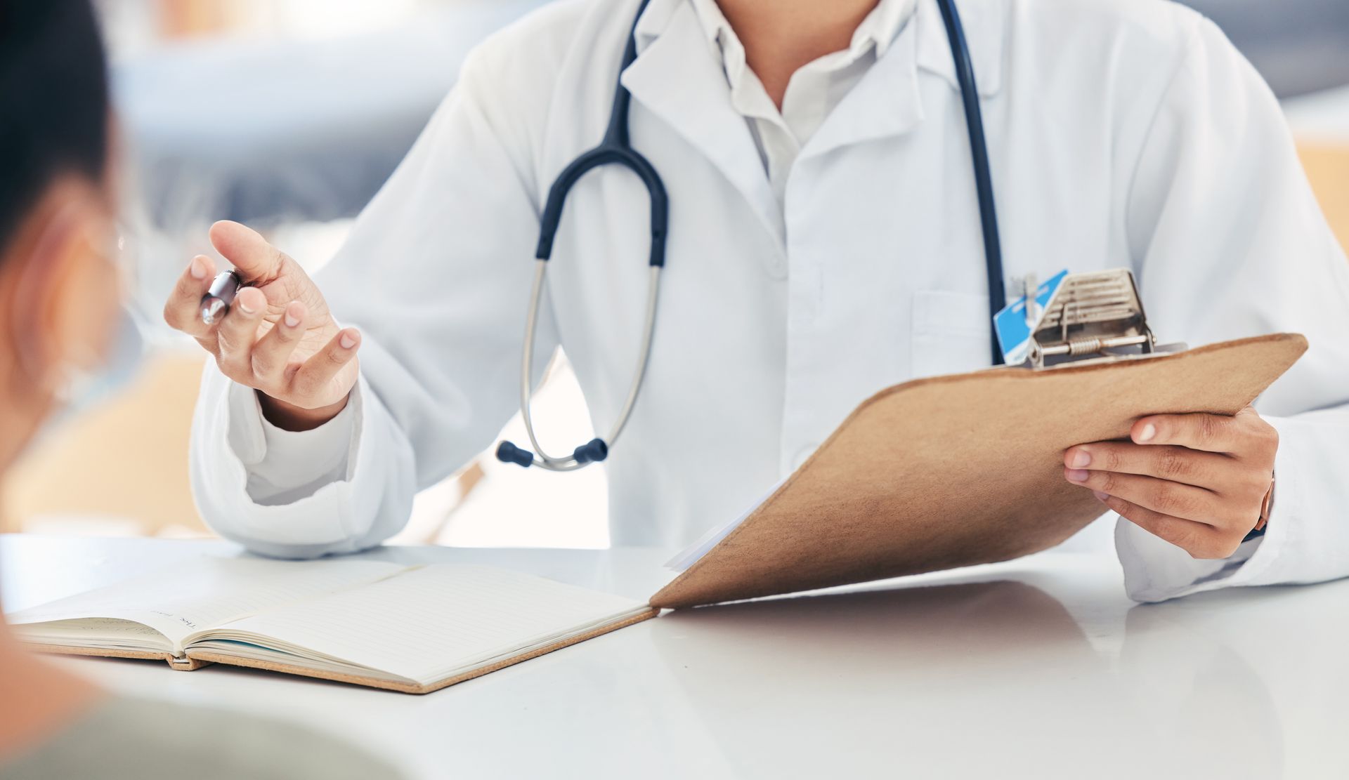 Doctor in white coat with stethoscope, points at clipboard, speaking with patient. Doctor in white coat with stethoscope, points at clipboard, speaking with patient.