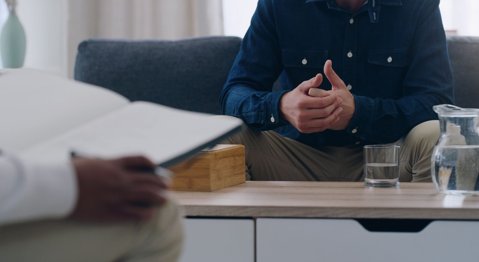 Man in blue shirt, hands clasped, talking to person holding open notebook on a couch. Man in blue shirt, hands clasped, talking to person holding open notebook on a couch.
