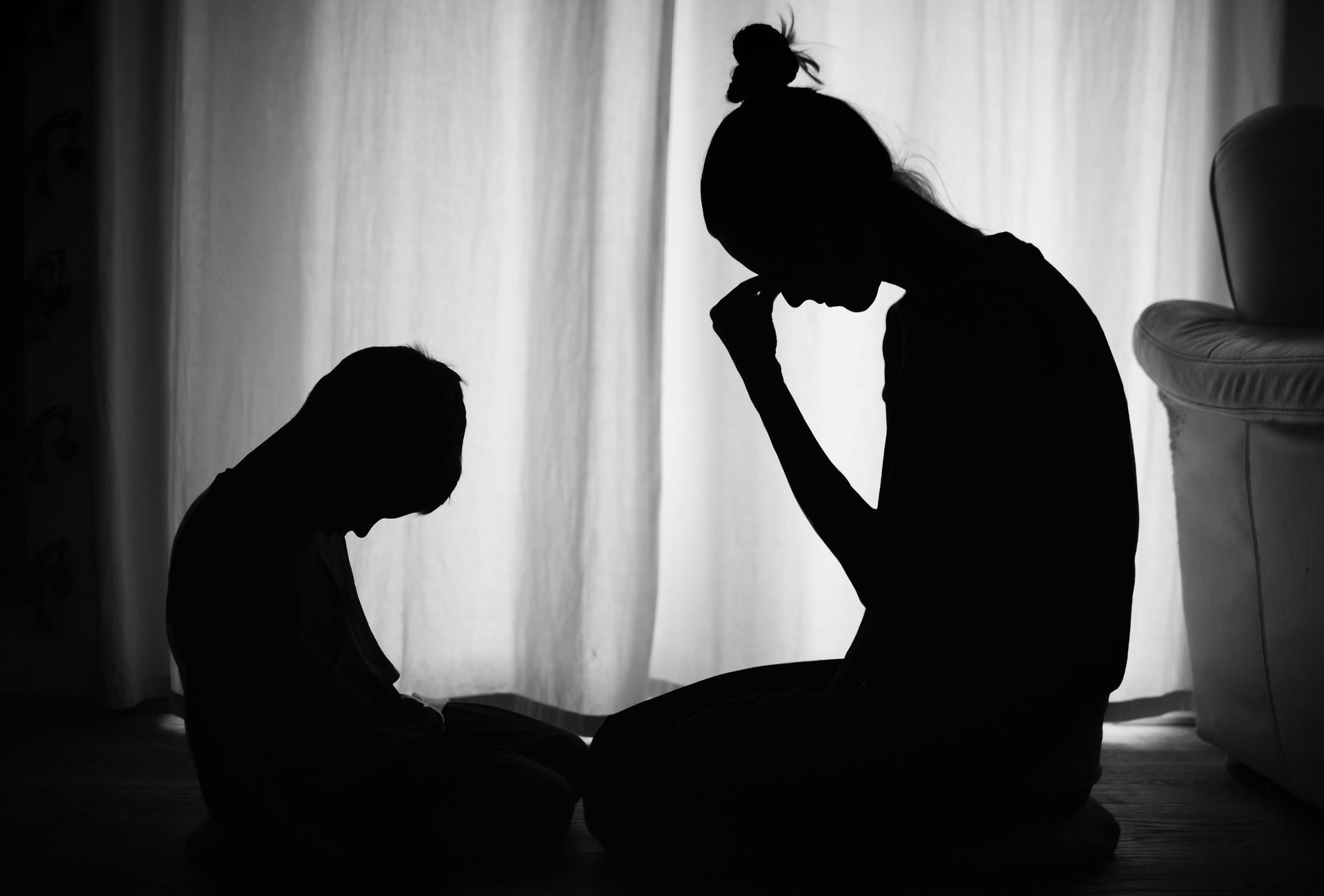 Silhouette of two people, one appearing to be an adult, and one a child, sitting and bowed down in front of a curtain. Silhouette of two people, one appearing to be an adult, and one a child, sitting and bowed down in front of a curtain.
