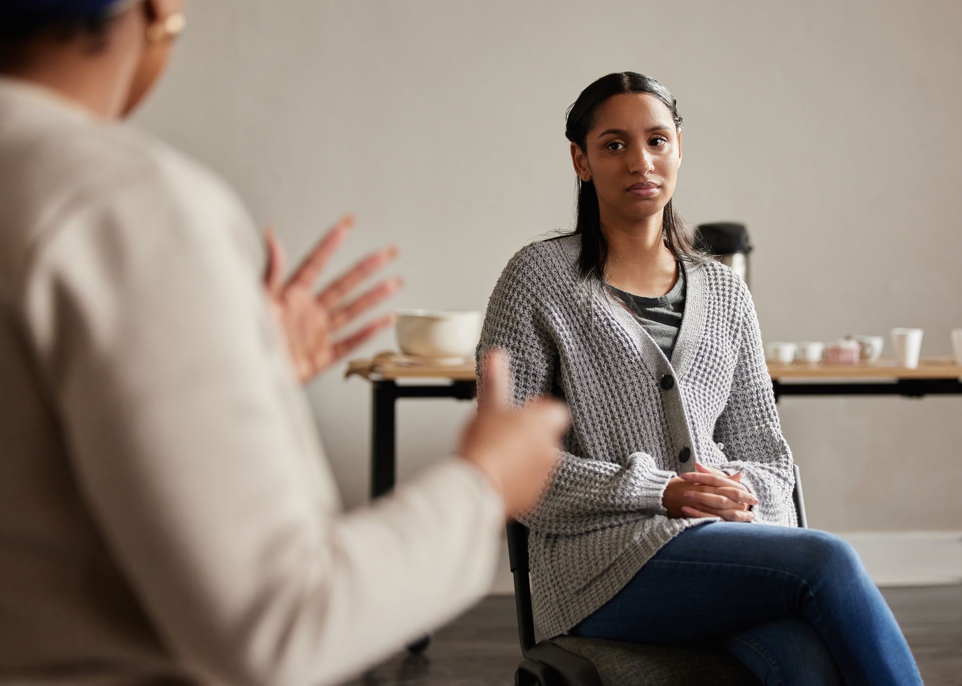 Woman in therapy session, sitting and listening to person speaking, both in a brightly lit room. Woman in therapy session, sitting and listening to person speaking, both in a brightly lit room.