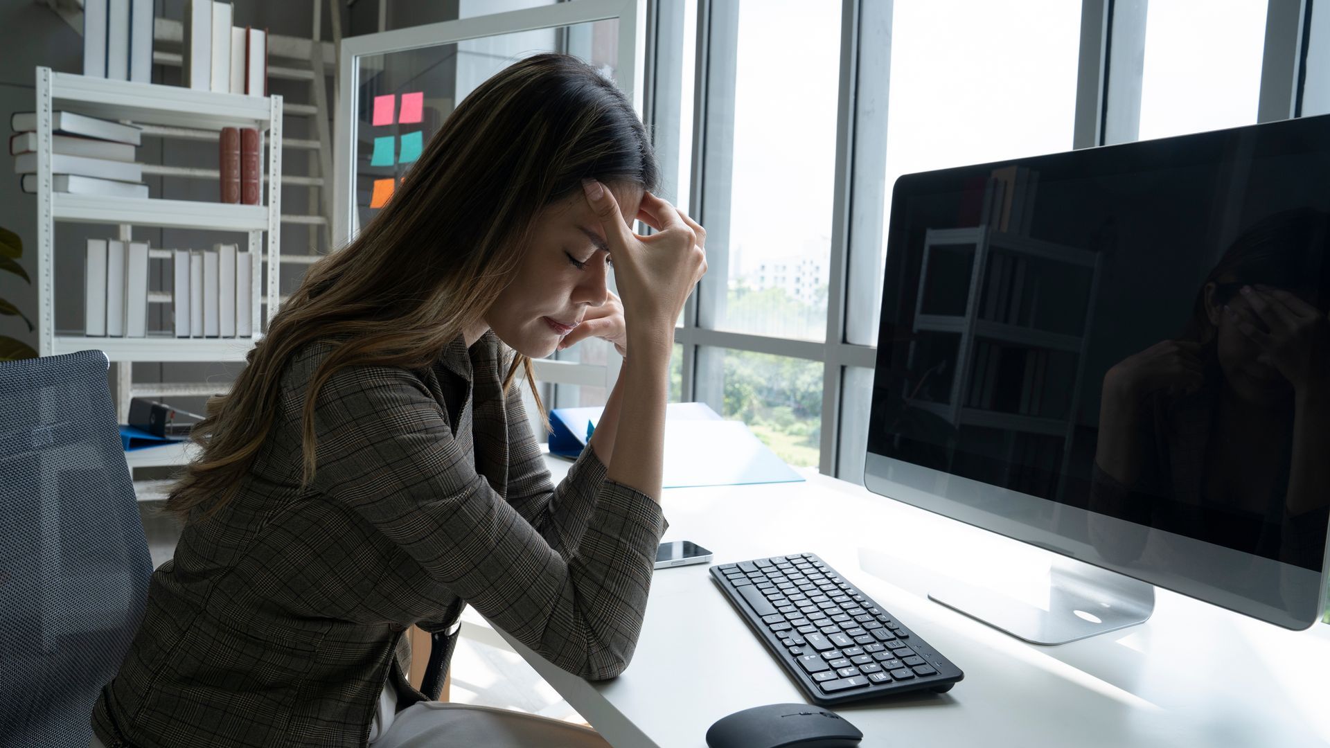 Woman at desk with head in hand, looking stressed near computer.