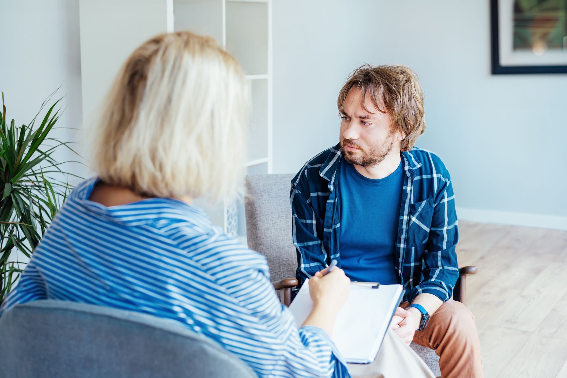 Therapist and patient in a counseling session; patient looks concerned, therapist takes notes. Therapist and patient in a counseling session; patient looks concerned, therapist takes notes.