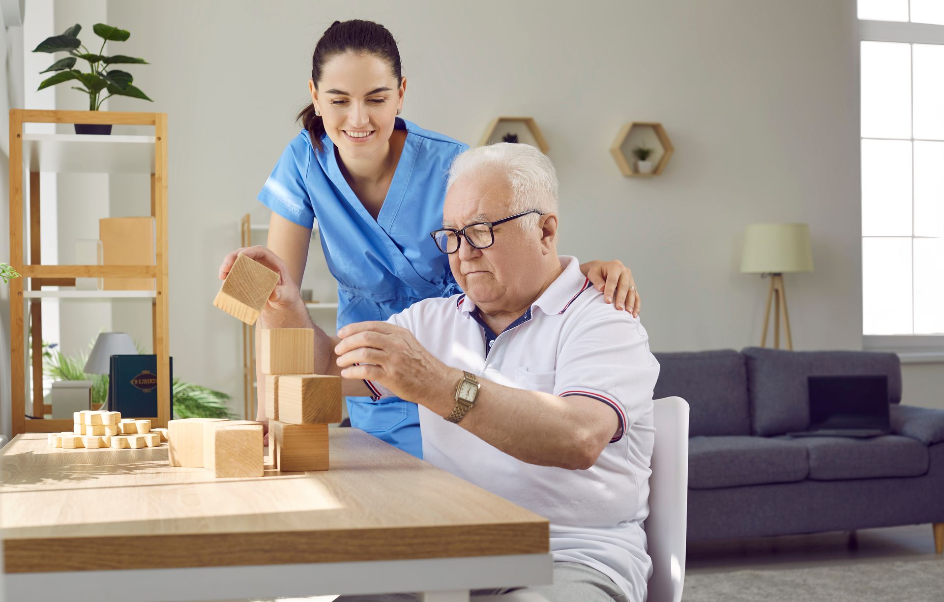 Woman in blue uniform assisting a man with glasses to stack wooden blocks at a table. Woman in blue uniform assisting a man with glasses to stack wooden blocks at a table.