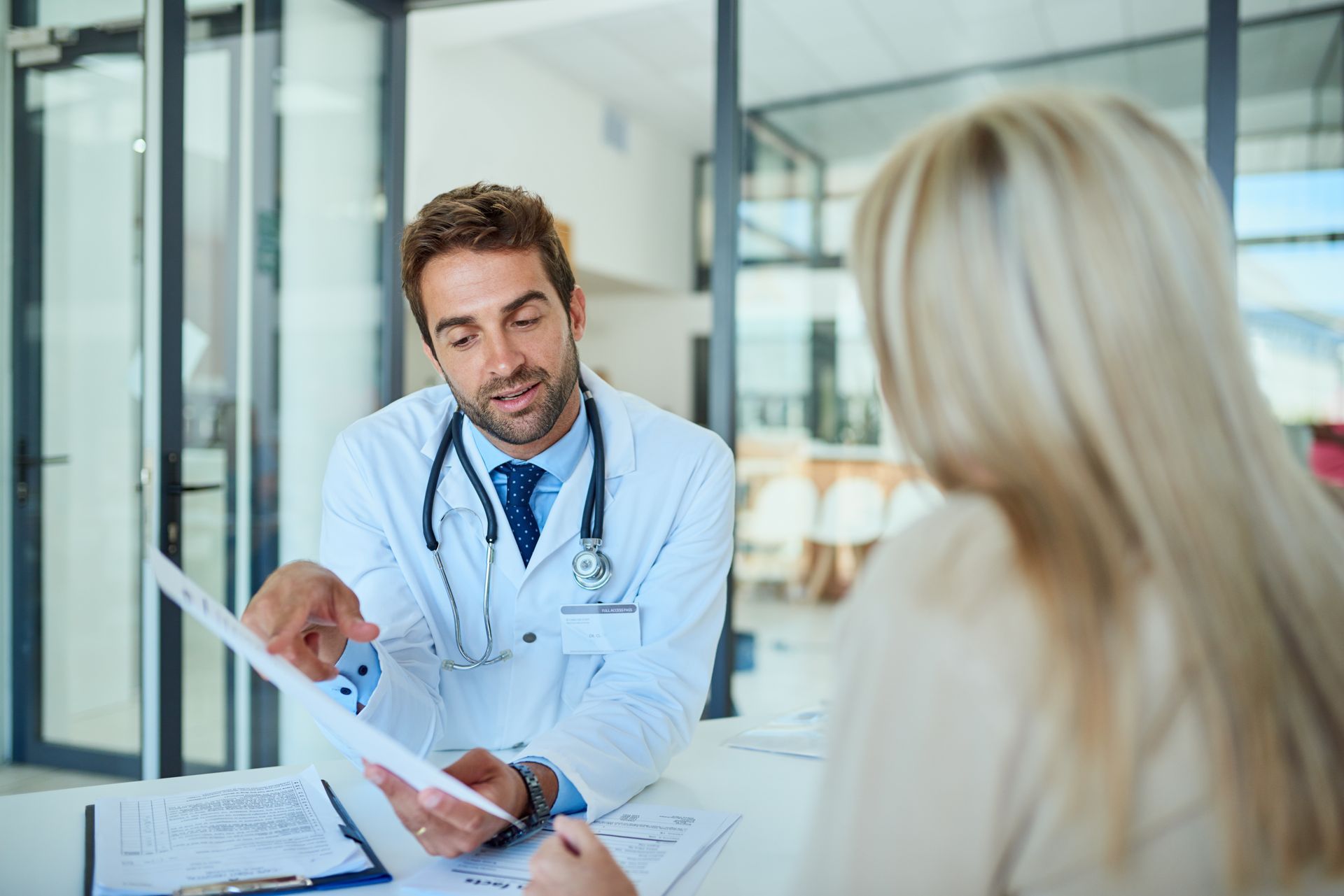 Doctor in lab coat pointing at paperwork, discussing results with a patient in an office. Doctor in lab coat pointing at paperwork, discussing results with a patient in an office.