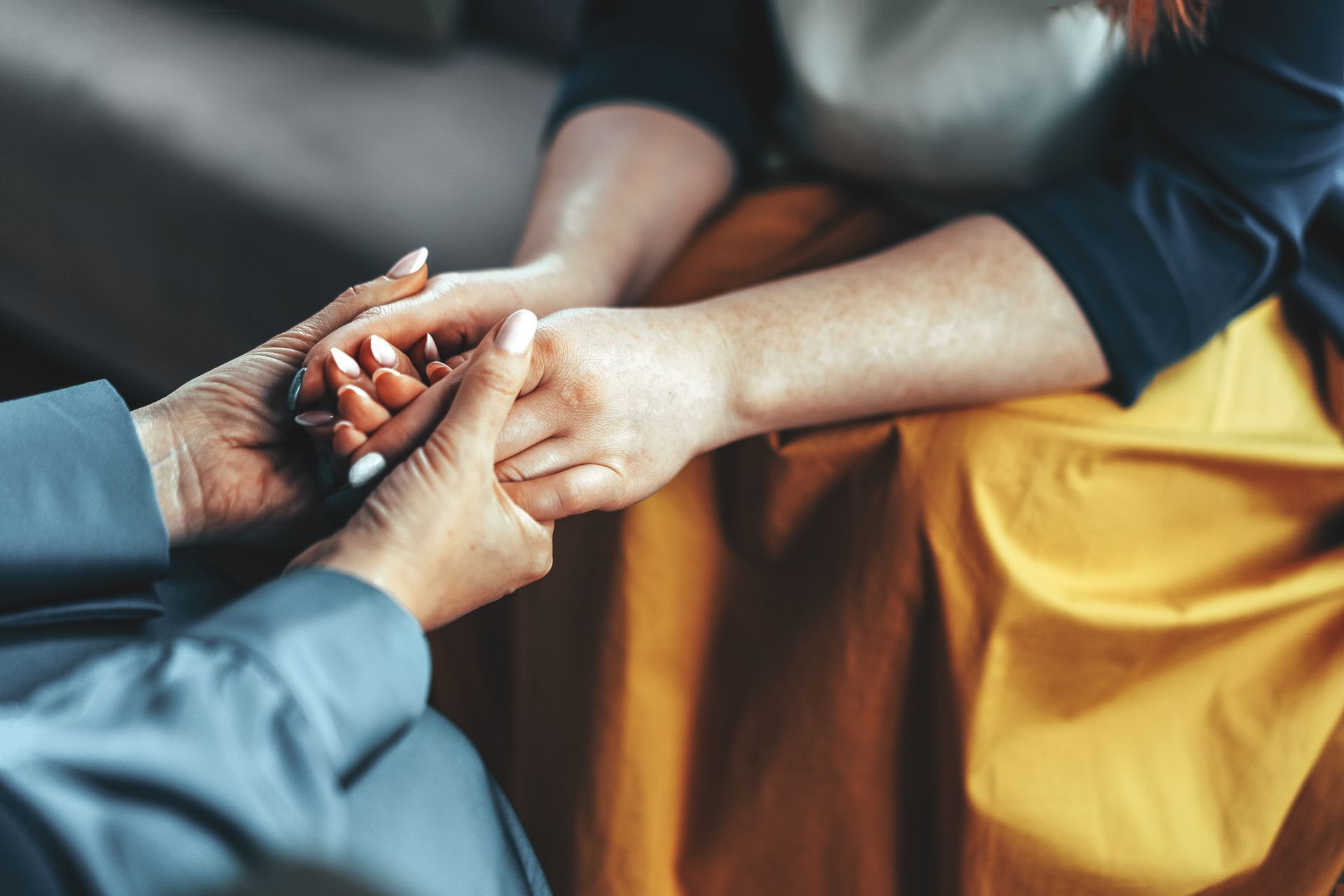 Hands clasped in support, one person in blue, the other in yellow. Hands clasped in support, one person in blue, the other in yellow.