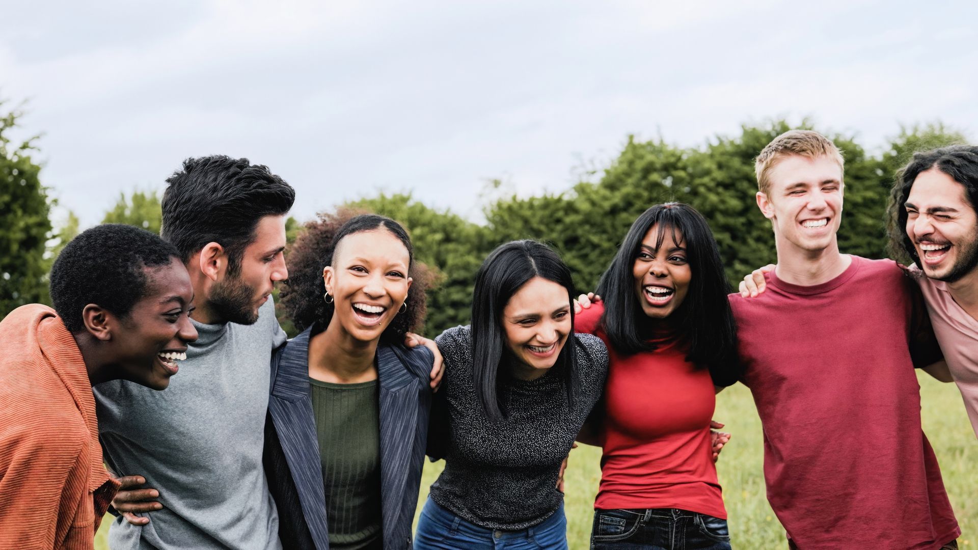 A group of people with arms around each other laughing in a field. A group of people with arms around each other laughing in a field.