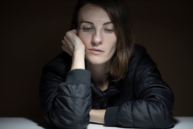 Woman with head resting on hand, looking down, dark setting.
