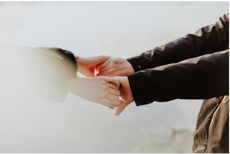 Two hands holding each other, one in a black jacket, with a blurred background.