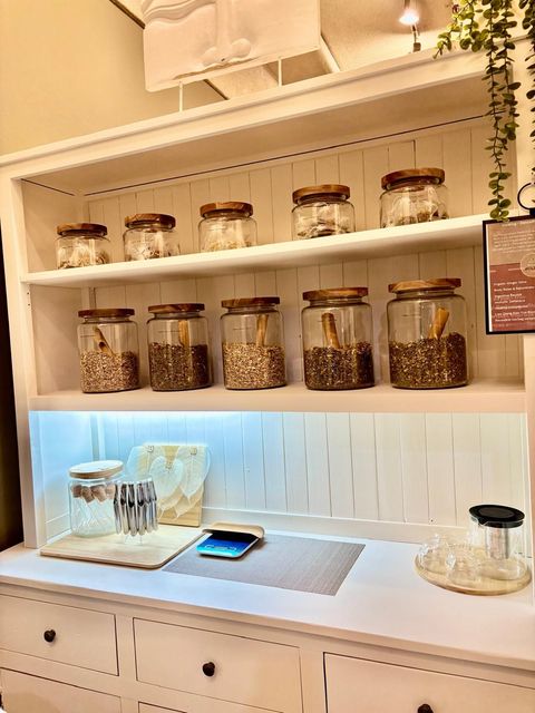 White cabinet with jars of ingredients, wooden lids, and small appliances on the countertop.