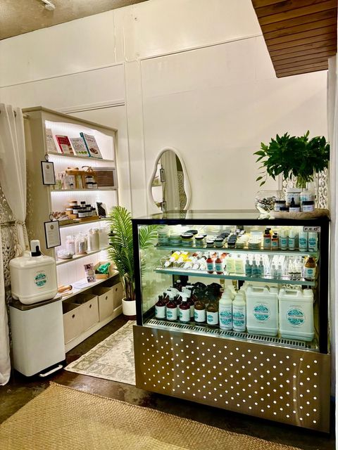 Small shop interior with a display case, shelves, and a large plant.