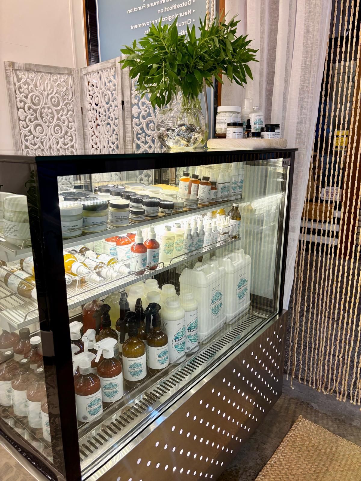 A refrigerated display case filled with natural cleaning and skincare products in a shop setting.
