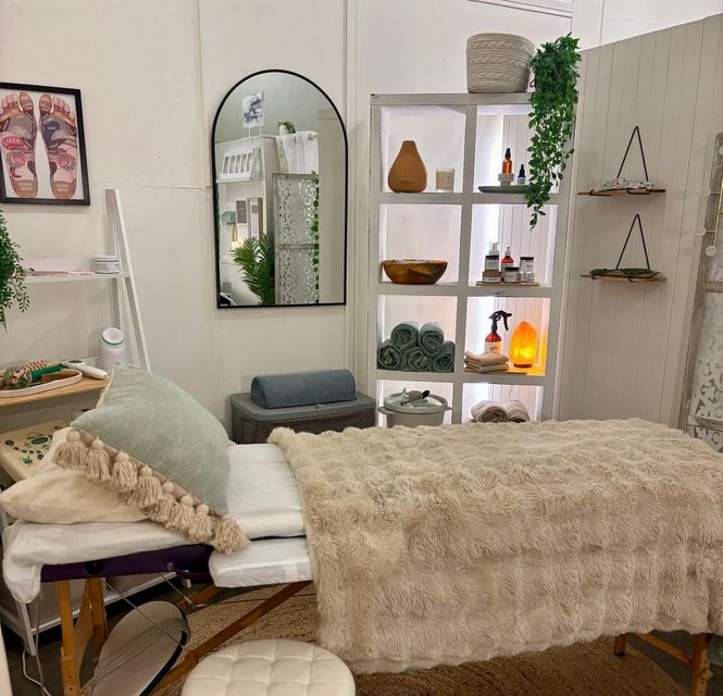 Massage therapy room with massage table, shelving, and decorations; soft lighting and neutral tones.