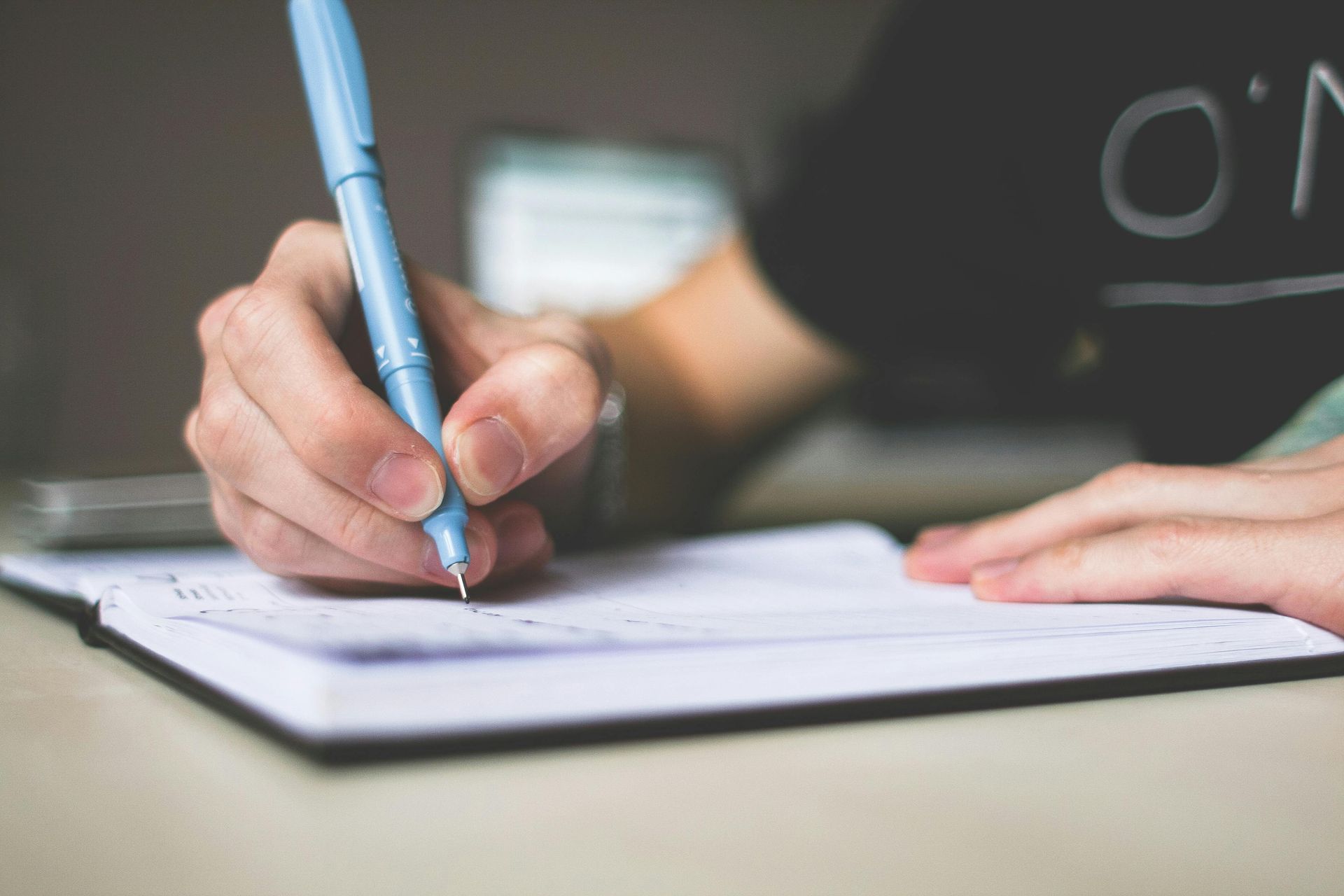 Person writing in a notebook with a blue pen; close-up shot.