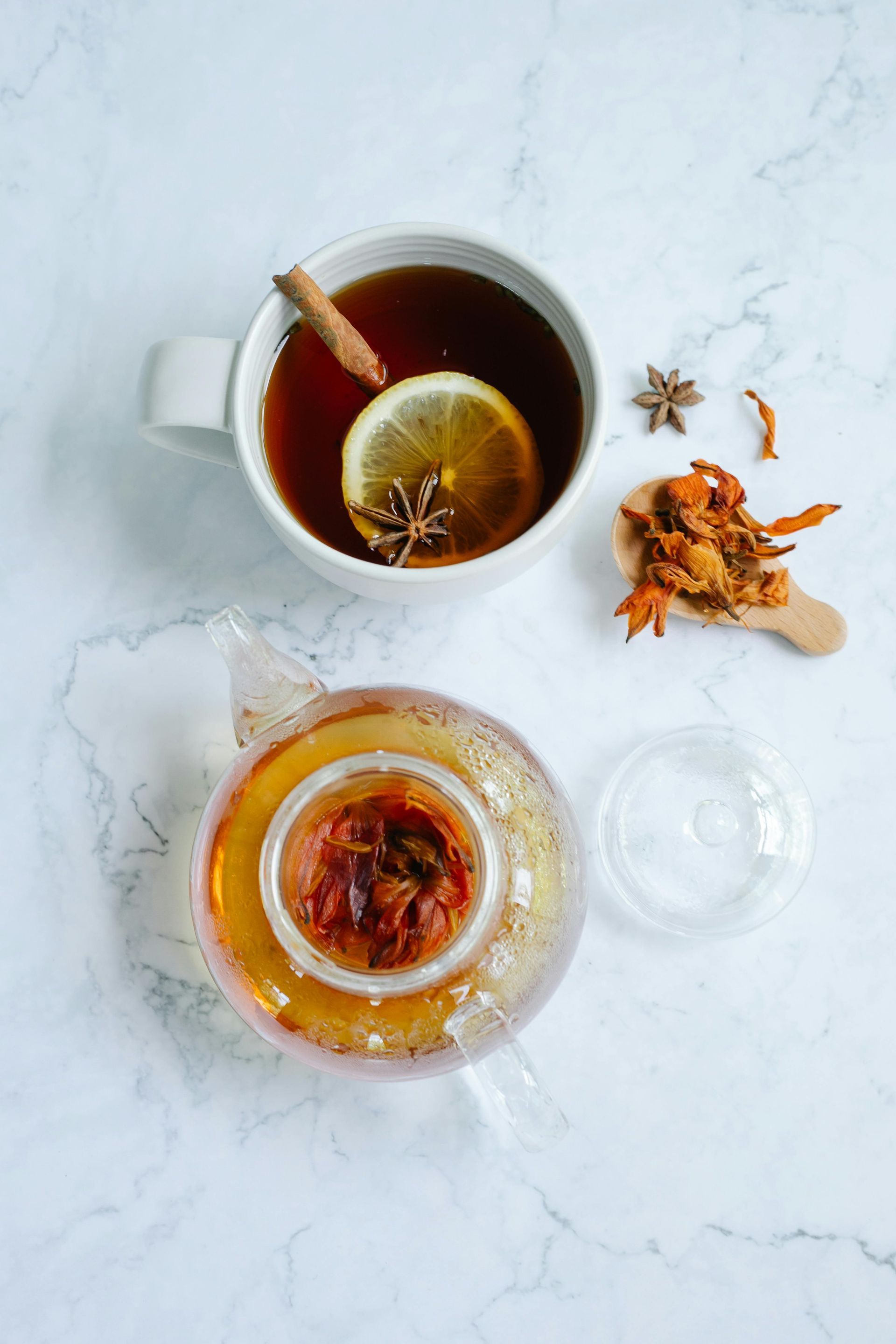 Cup of tea with lemon and spices, teapot on marble surface.