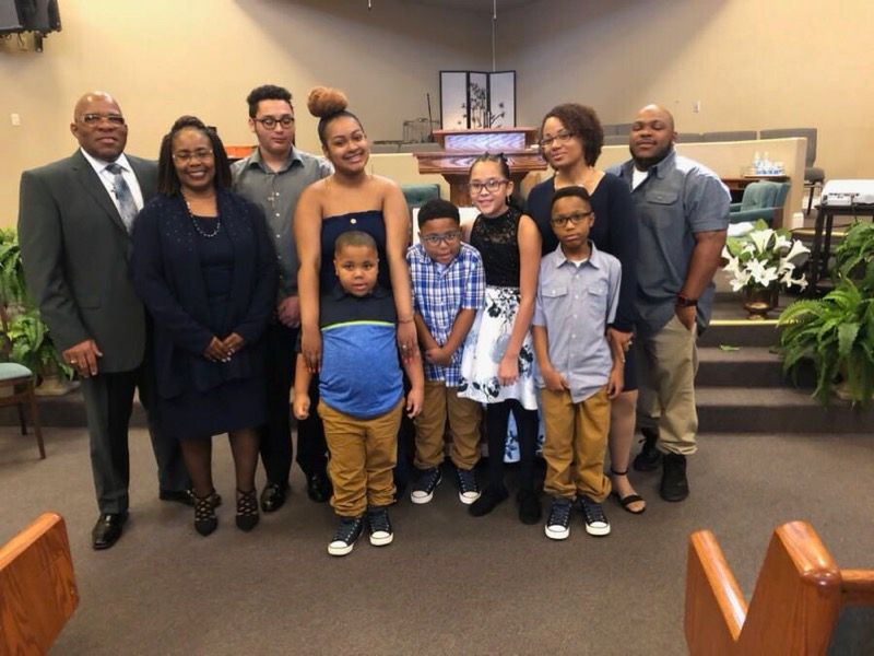 A diverse group of ten people stand together in a church sanctuary, posing for a group portrait.