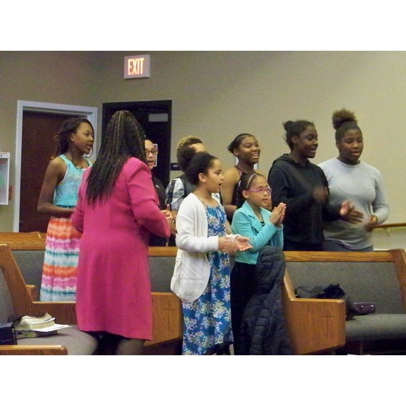 A group of people singing and clapping inside a church building with wooden pews.