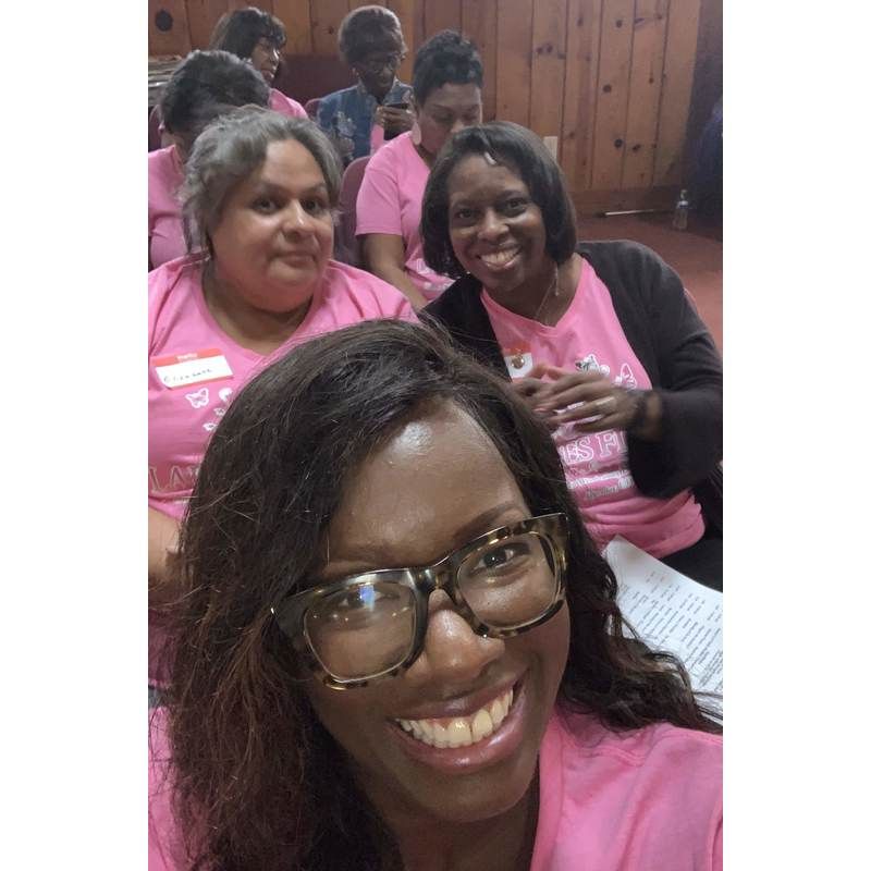 A group of people wearing pink shirts posing for a selfie in a room with wood-paneled walls.