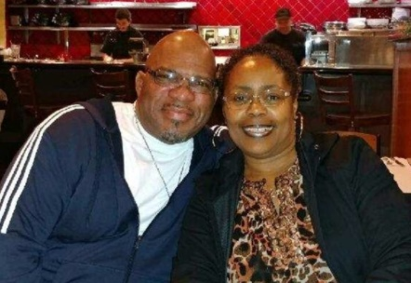 A couple smiles closely for a selfie inside a restaurant with a red, tiled wall in the background.