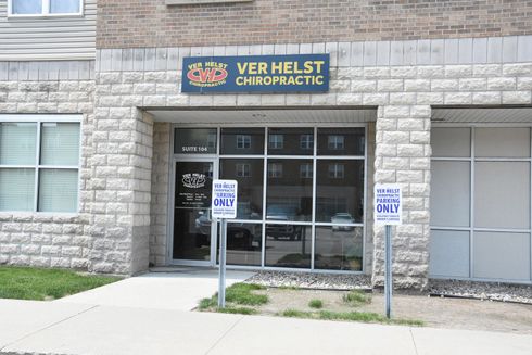 Exterior of Ver Helst Chiropractic office building with stone facade. Glass front entrance. Handicap parking signs present.