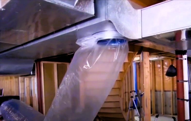 Basement ductwork during Aeroseal sealing process with clear plastic sheeting over vent and wooden stairs in background
