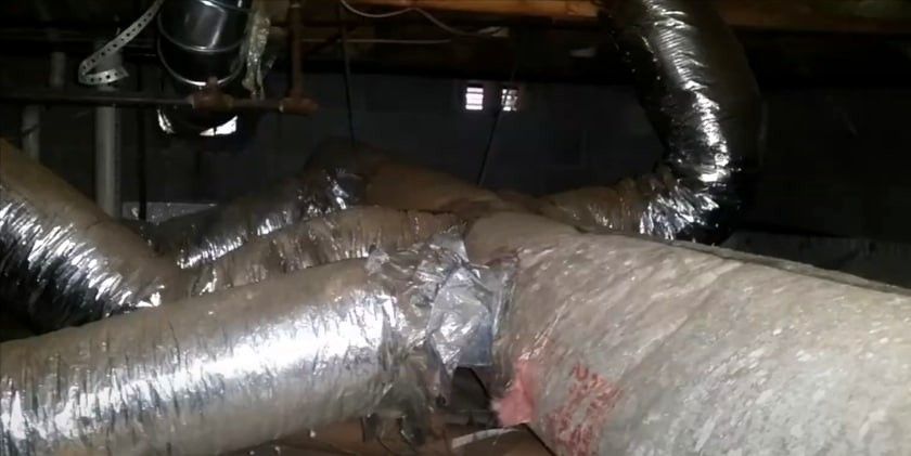 Damaged HVAC ductwork in a basement caused by pest infestation, showing torn insulation and rodent bite marks