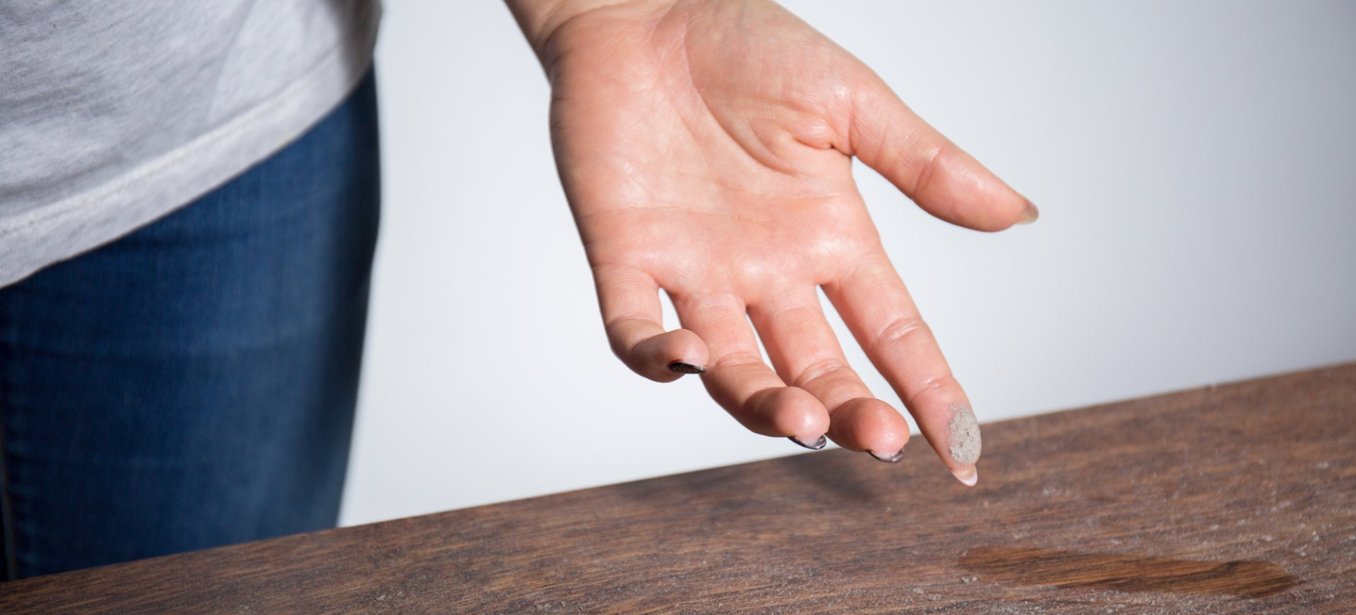 A woman's hand is showing dust that has collected on her table.