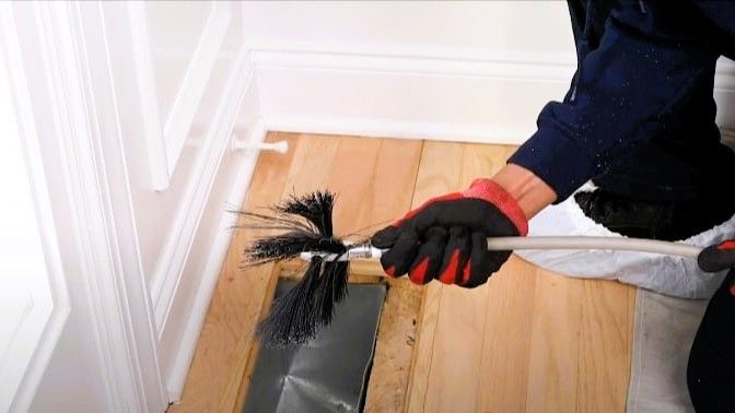 A person in gloves performs duct cleaning with a long brush.