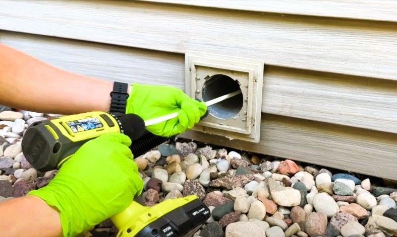 Expert cleaning vent with a drill, wearing green gloves