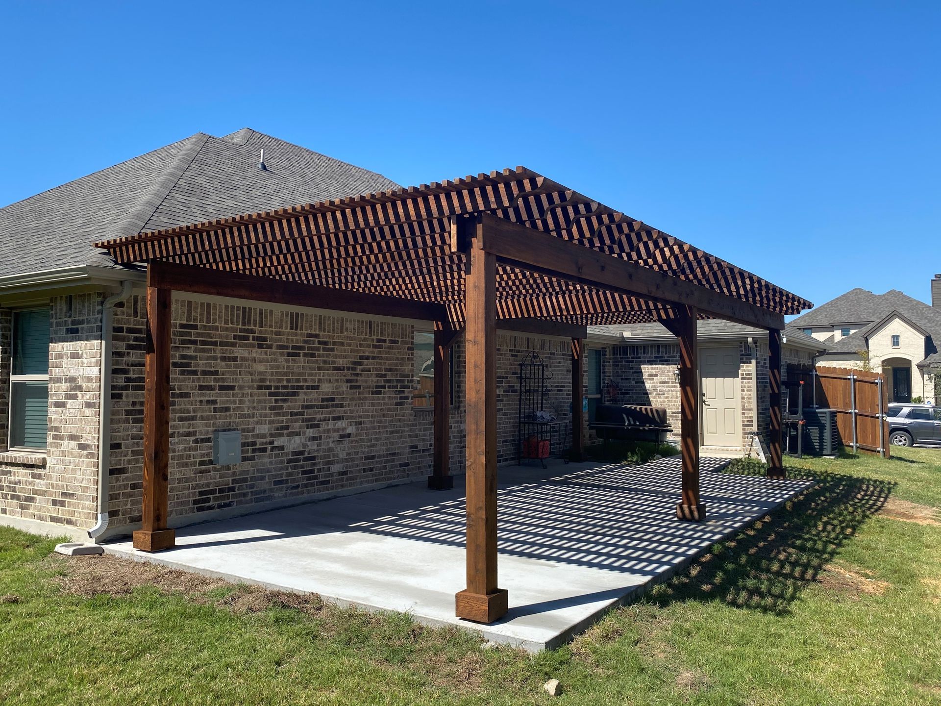 A wooden pergola is sitting in front of a brick house.