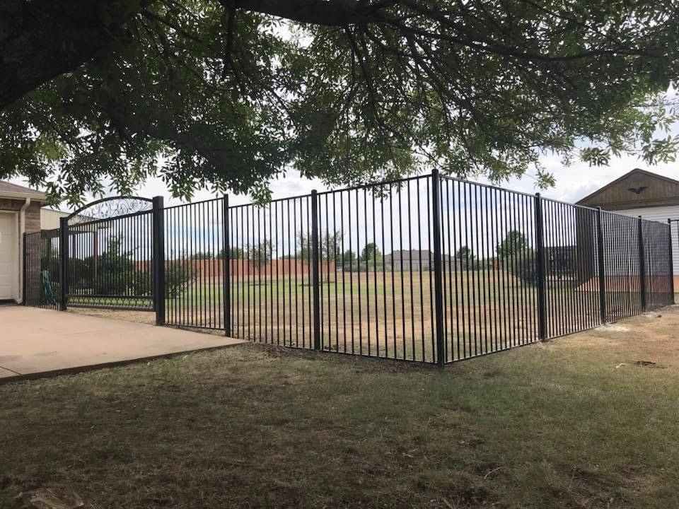 A metal fence is surrounding a field in front of a house.
