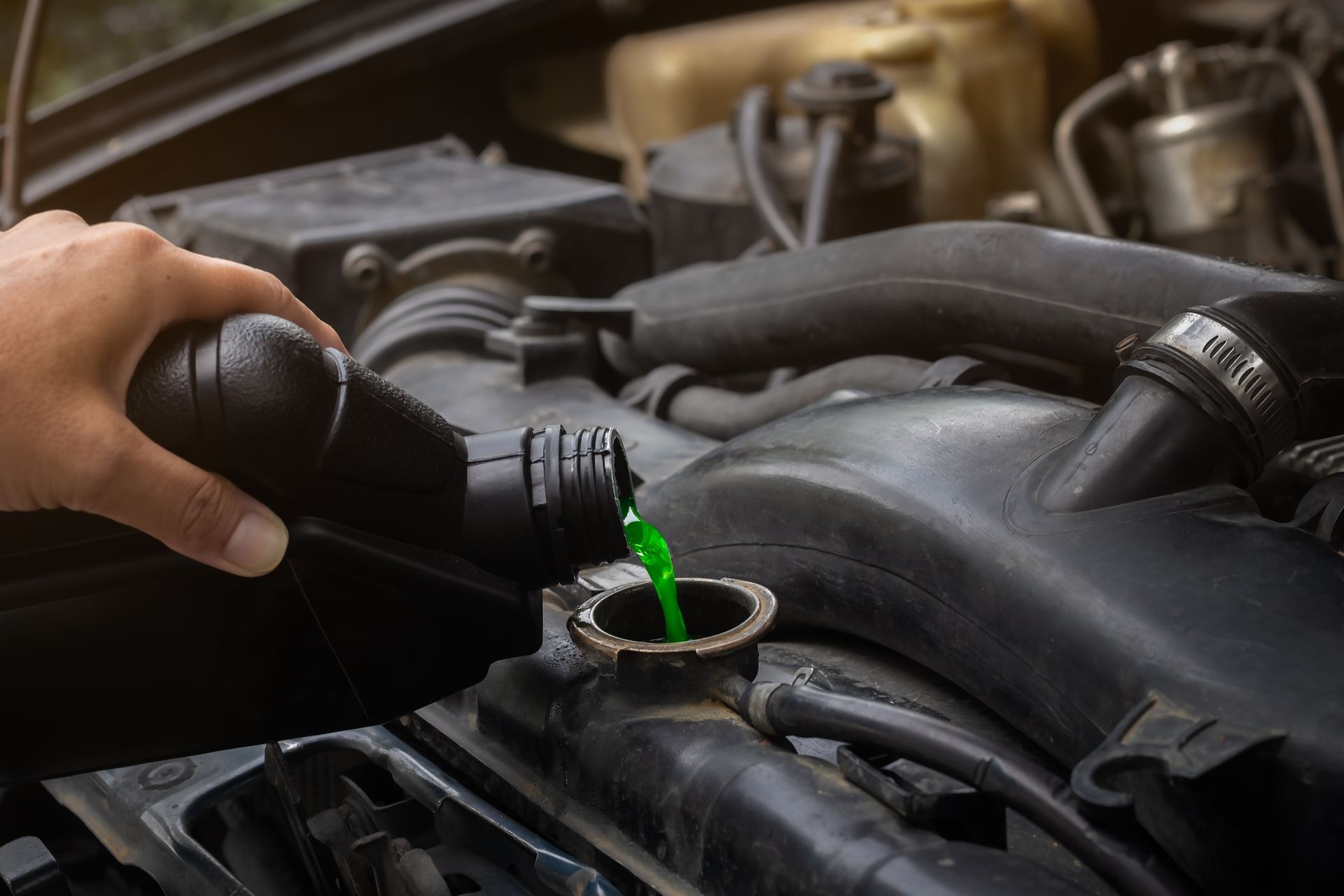 A hand pouring bright green engine coolant into the open radiator cap of a vehicle.