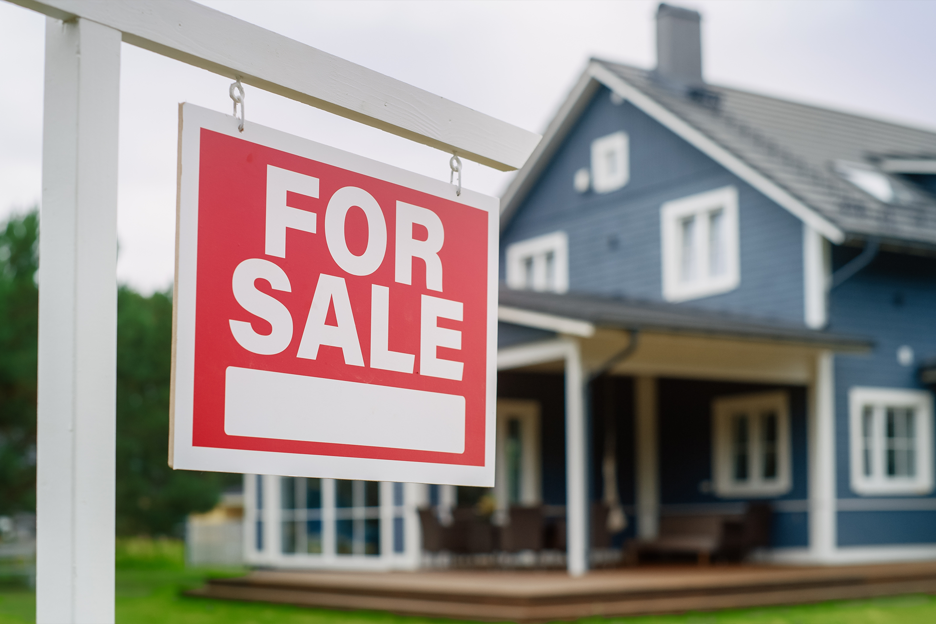 Red for sale sign in front of a blue house with a porch