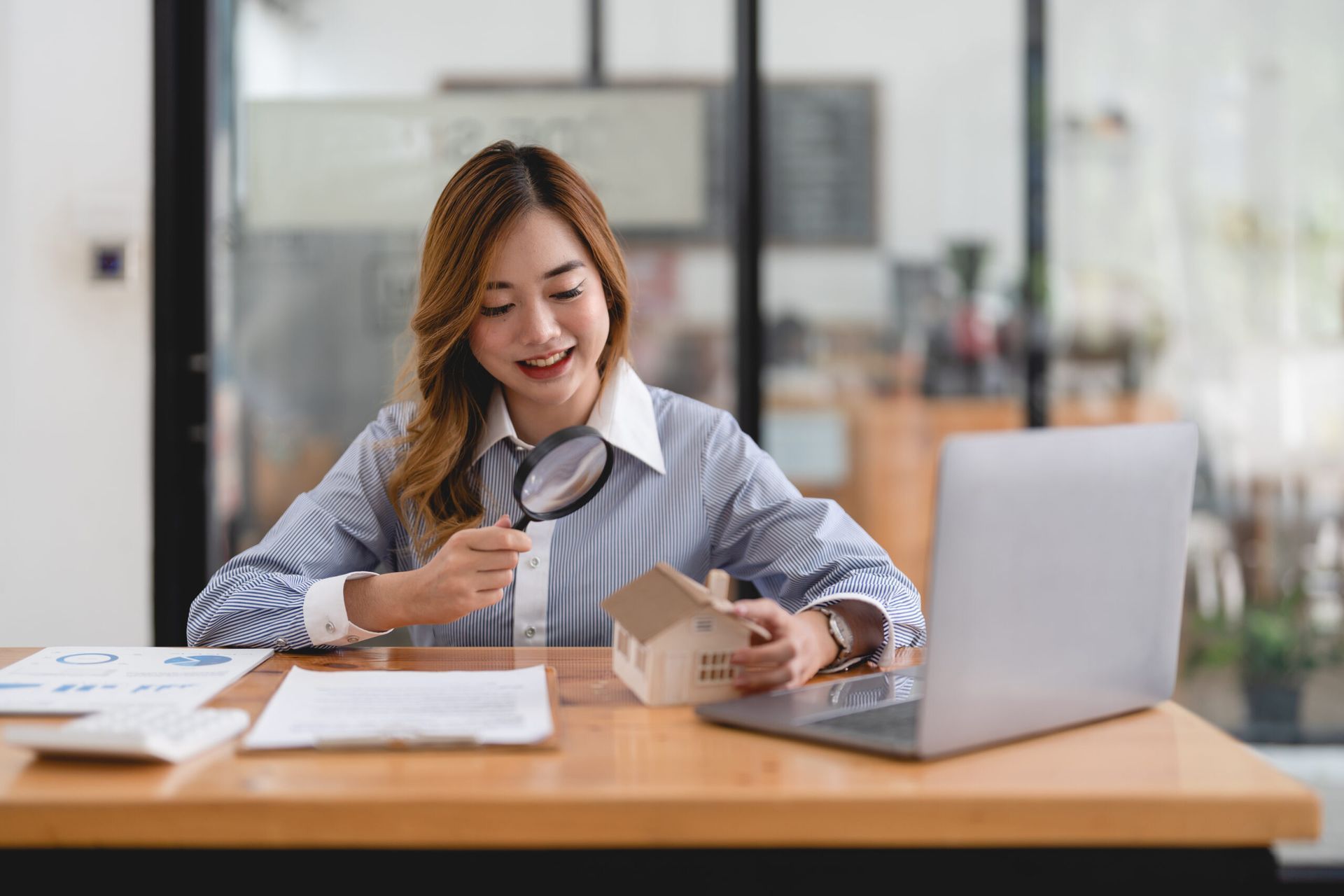 Woman at a desk packing a small box beside an open laptop, smiling in a bright office.