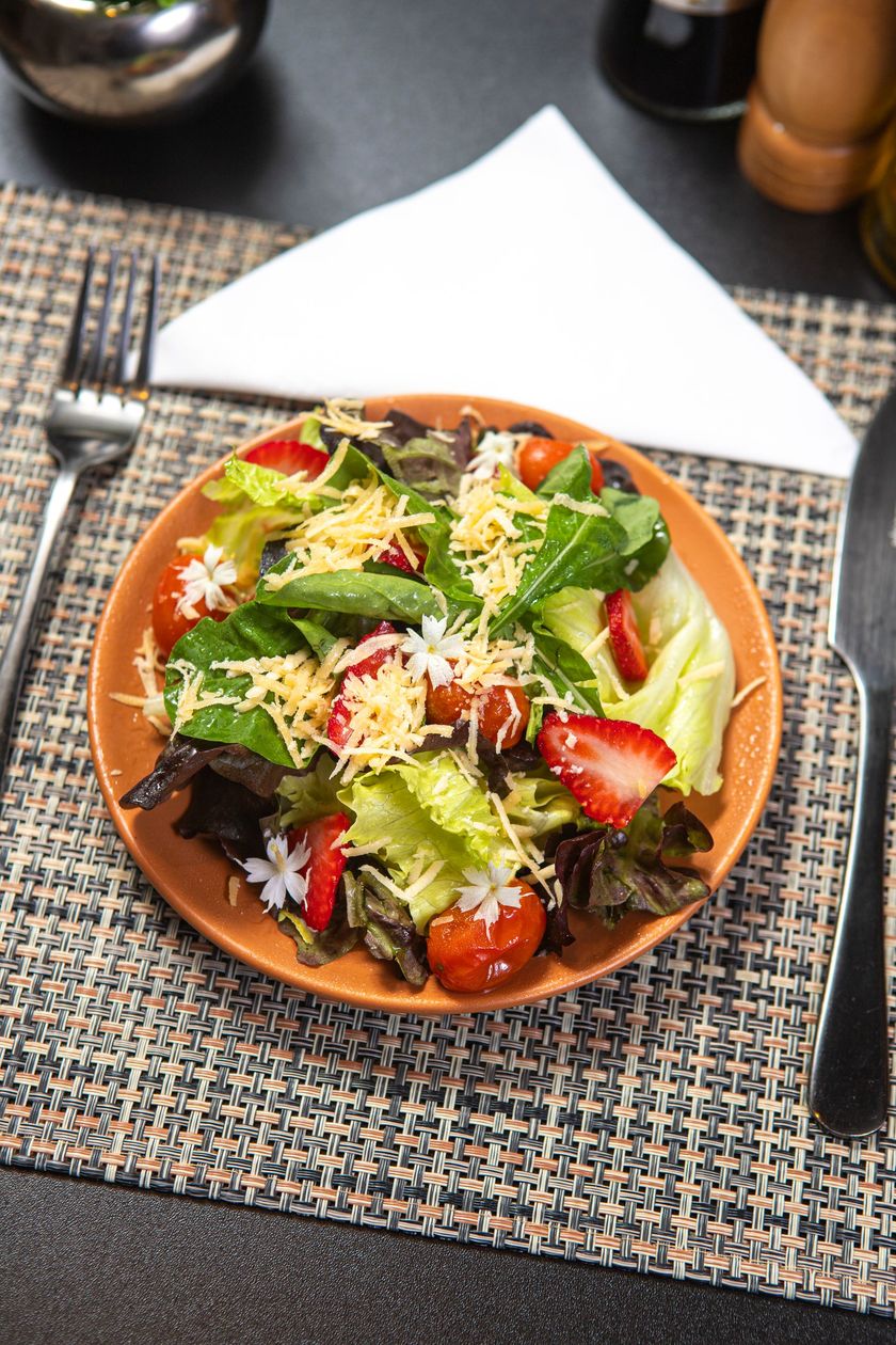 Uma salada com morangos, tomates, alface e queijo em um prato sobre uma mesa.