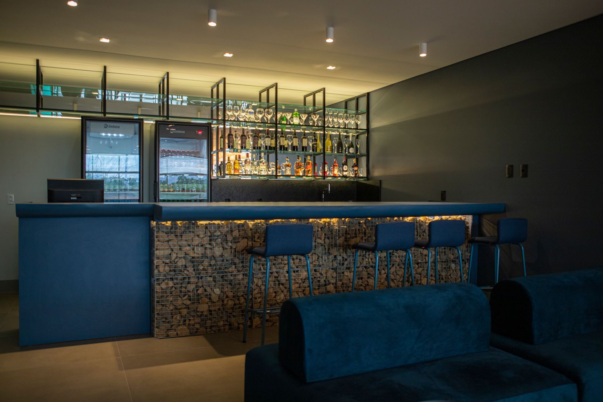 Uma sala de estar com um sofá azul e um bar ao fundo.