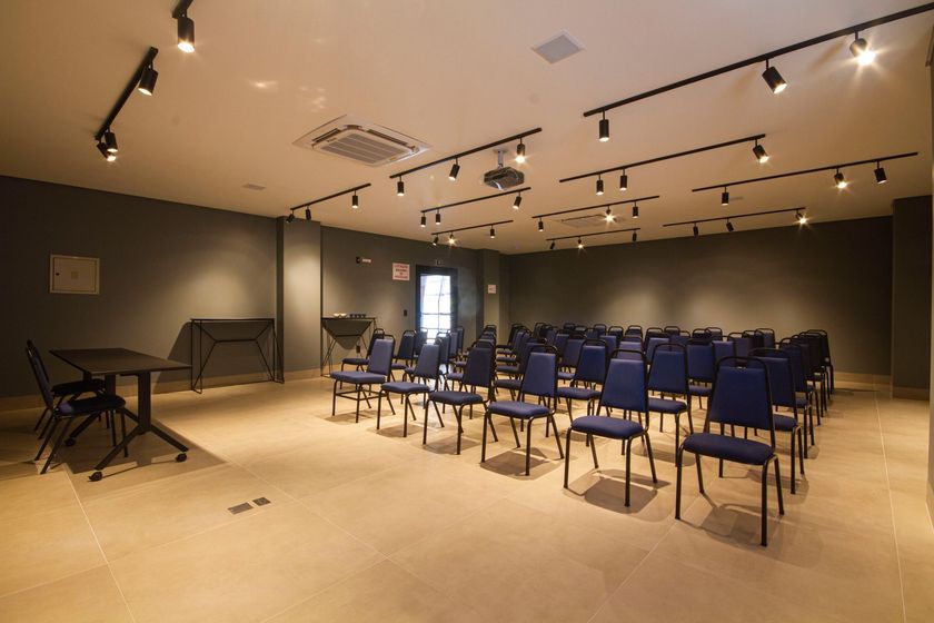 Uma sala grande com fileiras de cadeiras azuis e uma mesa.