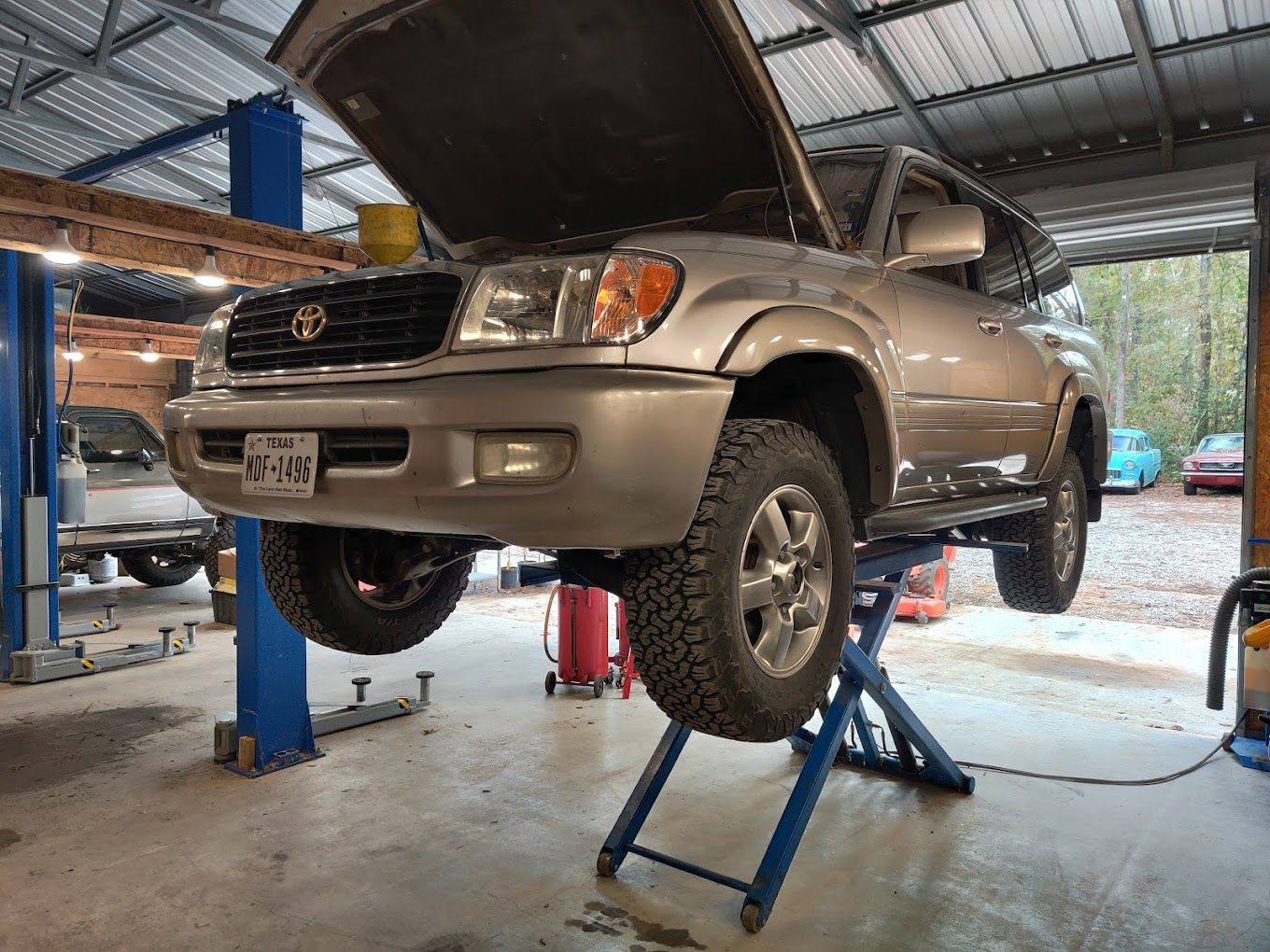 Silver Toyota Land Cruiser on a lift in a garage with the hood open. | Freedom Auto Repair