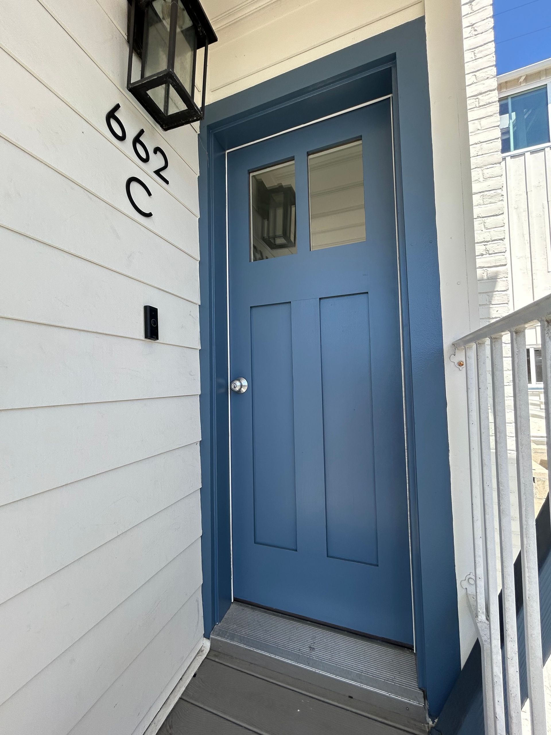 Blue front door with narrow windows at a house entrance, beside white siding and porch railing