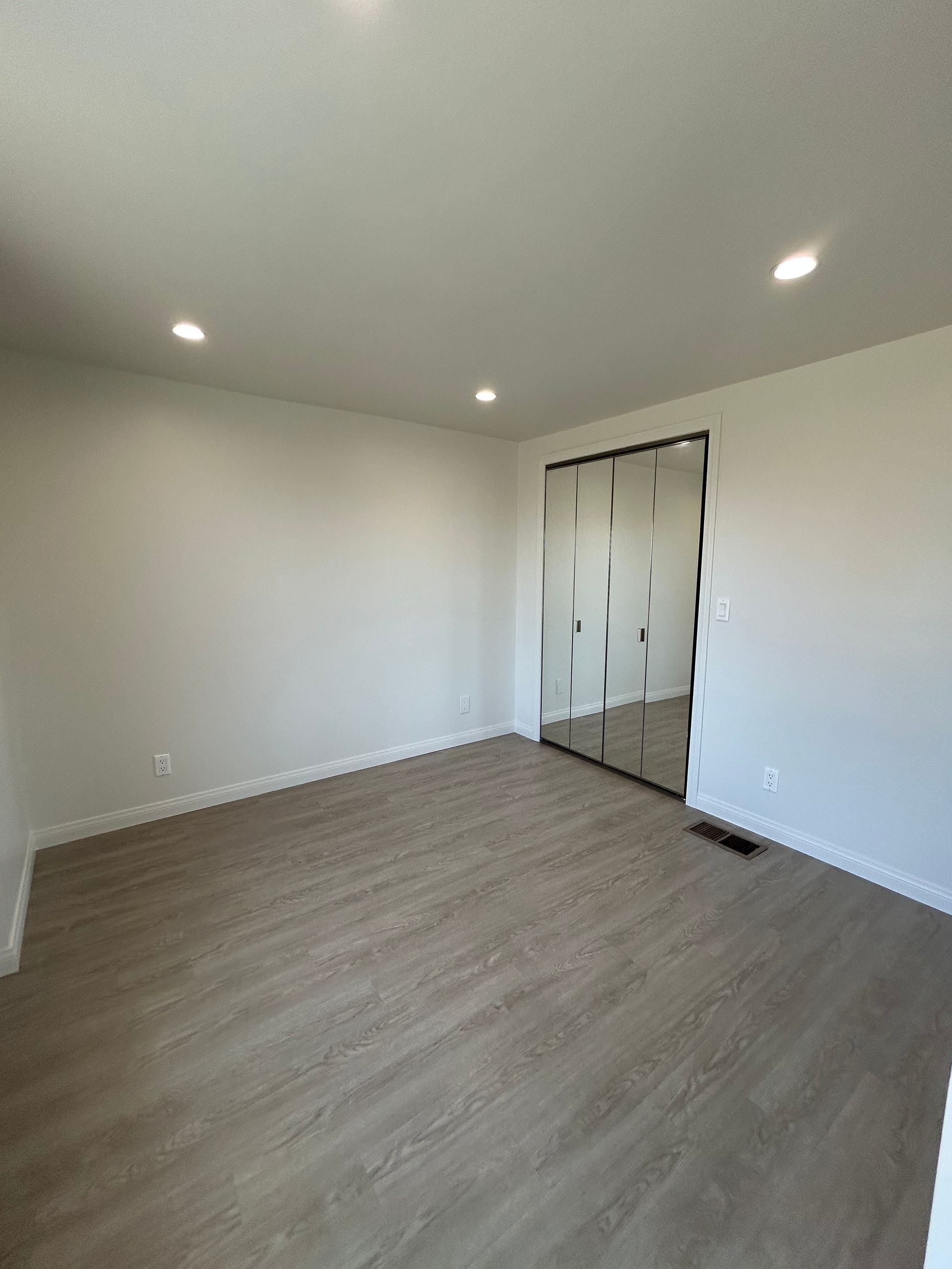 Empty white room with wood-look flooring, recessed lights, and an open doorway covered with plastic.