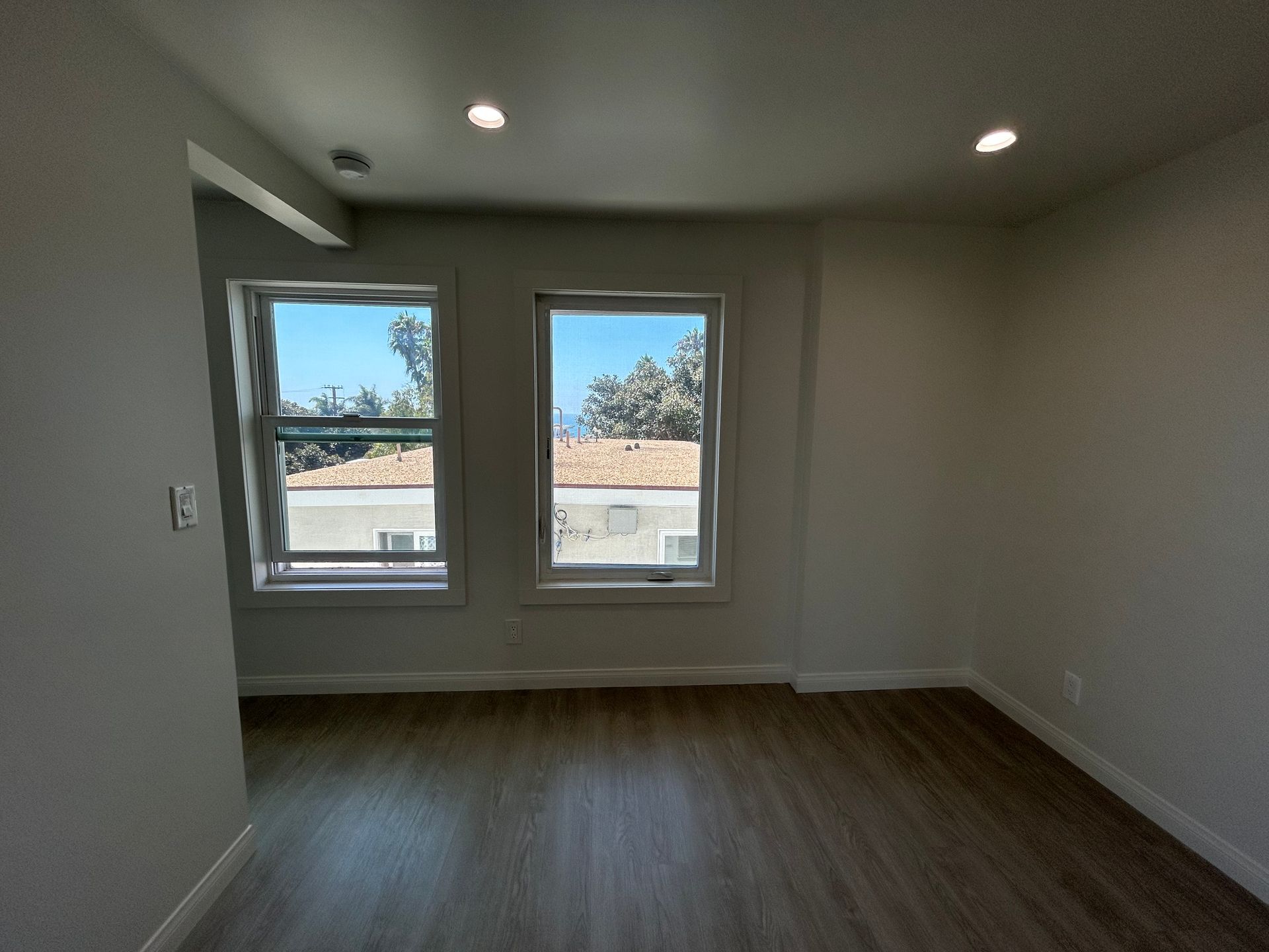 Empty room with gray walls, wood flooring, and two windows letting in daylight.