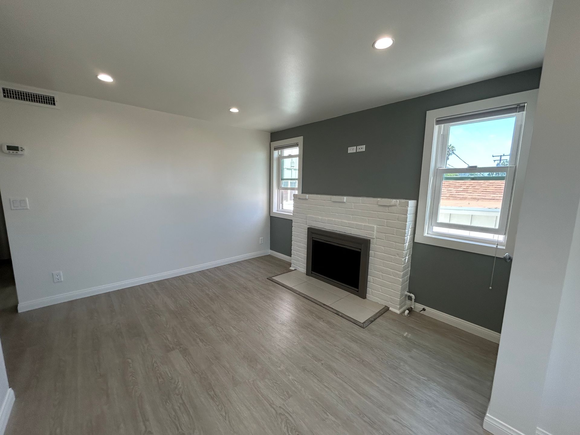Empty living room with gray accent wall, fireplace, windows, and light wood flooring