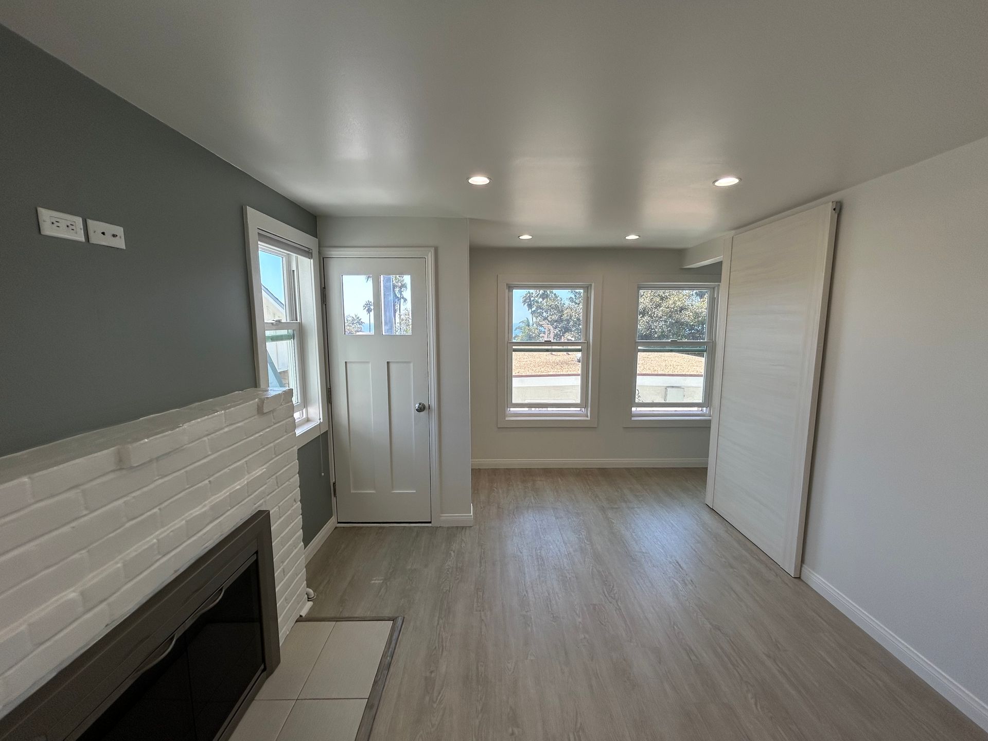 Empty modern living room with white walls, gray accent wall, fireplace, windows, and wood-look flooring