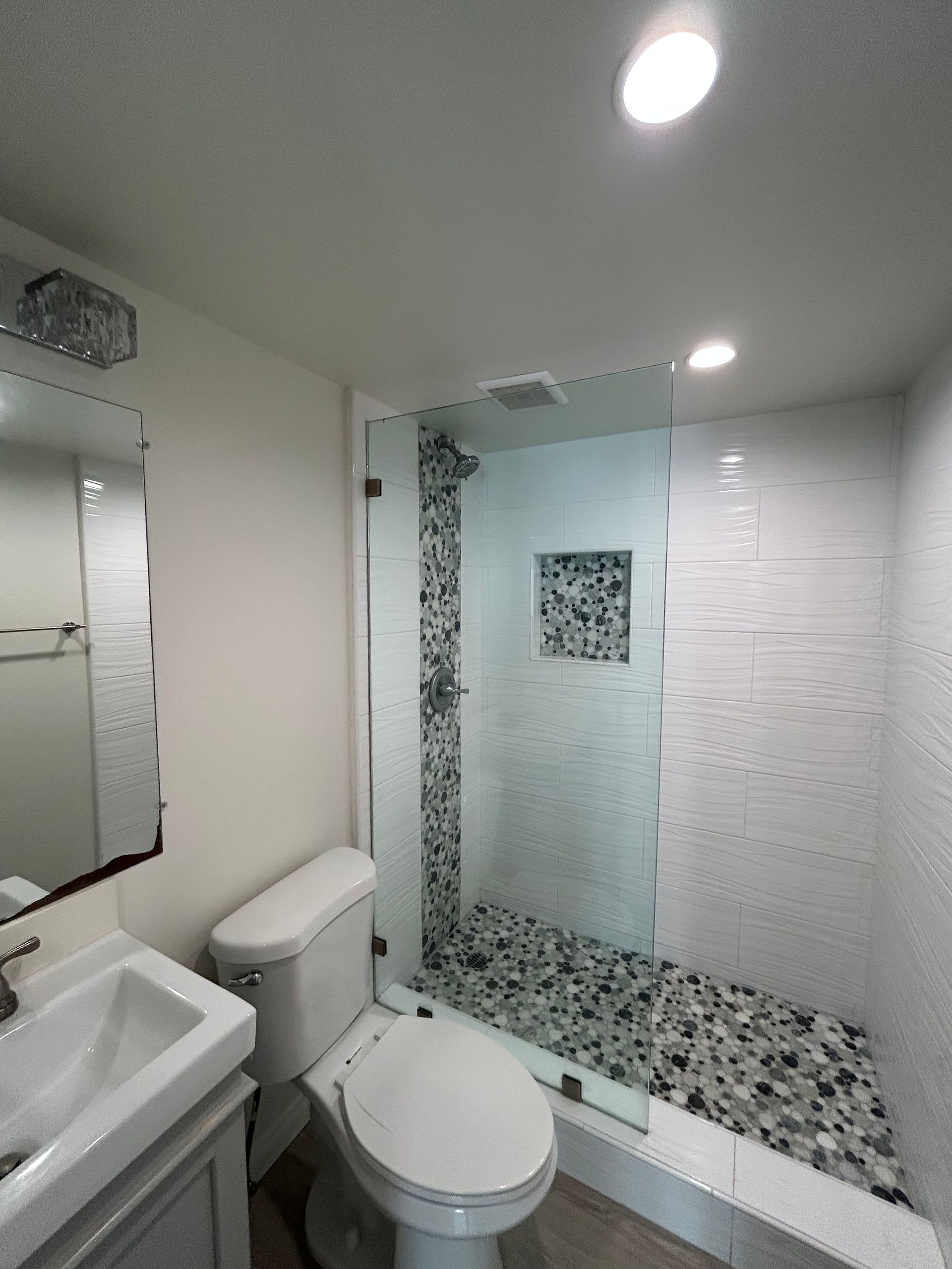 Modern bathroom with glass shower, toilet, sink, and bright recessed lighting