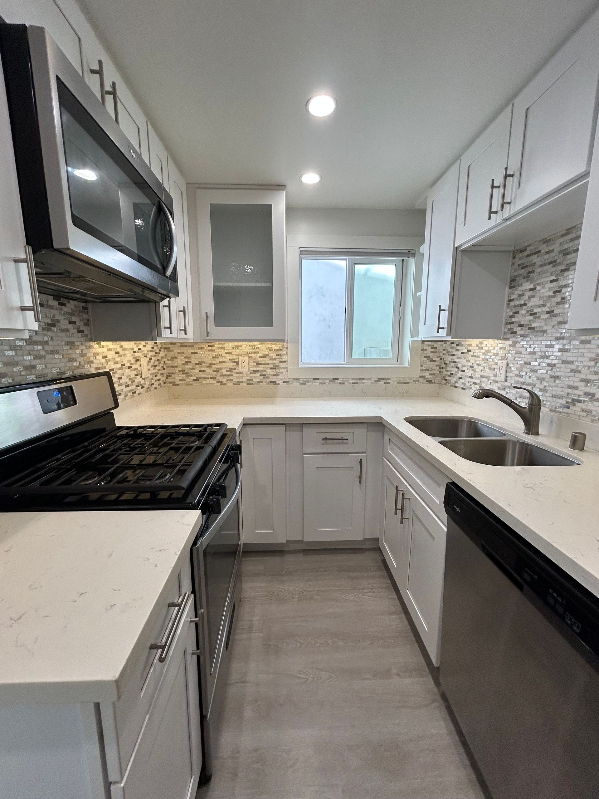 Modern white galley kitchen with stainless appliances, gray cabinets, and a mosaic tile backsplash
